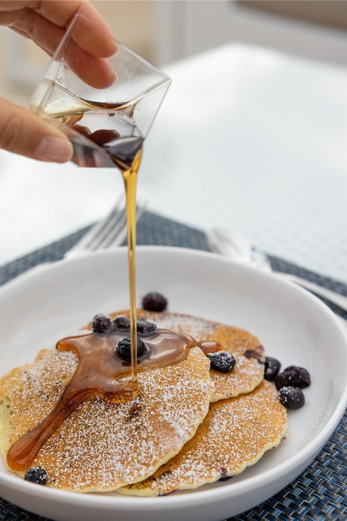 Maple syrup poured over blueberry pancakes on a white plate