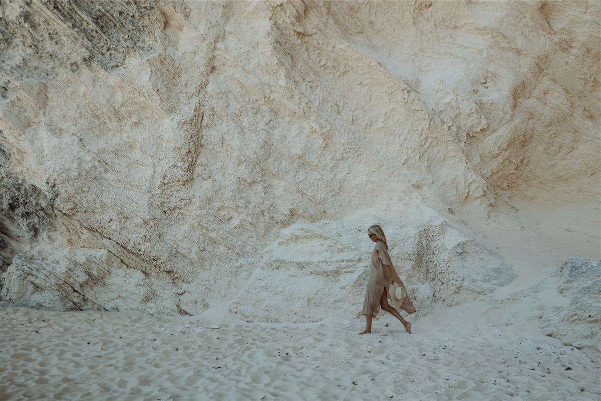 Model walking a wide sweep of pale sand beneath weathered white cliffs