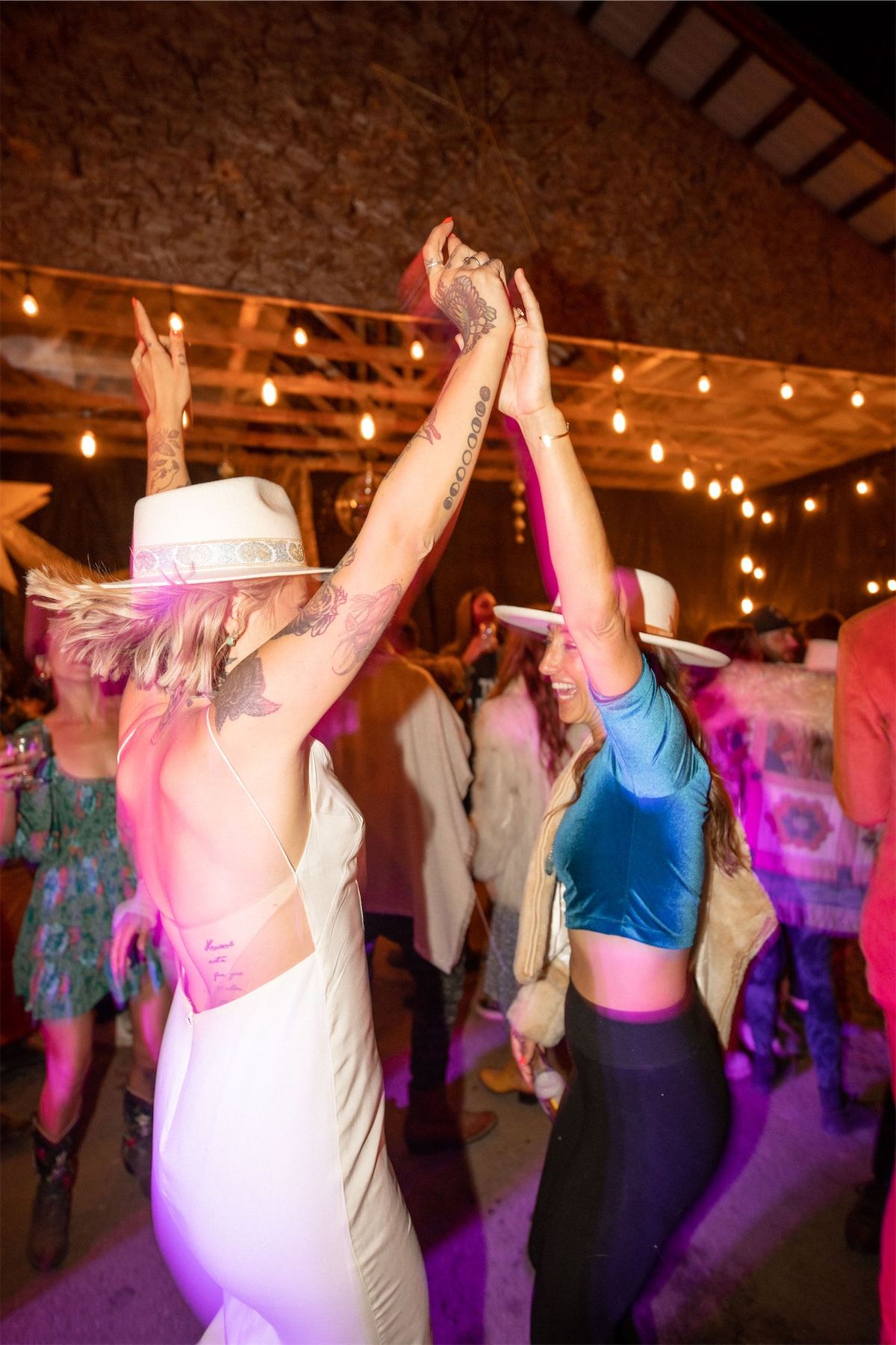 Bride dancing with arms raised under string lights in the barn reception