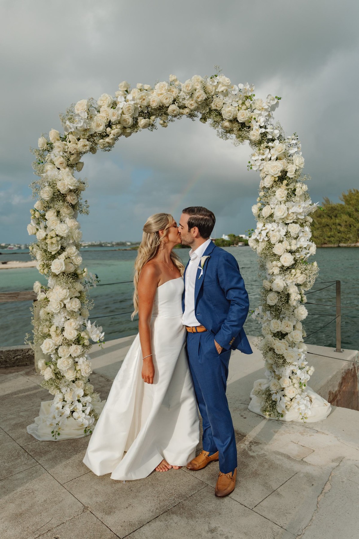 Paige and Cam kiss under the floral arch after the ceremony on Hawkins Island, Bermuda