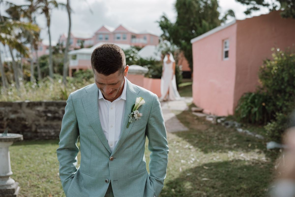 Groom waits with his head bowed as the bride walks up the garden path behind him