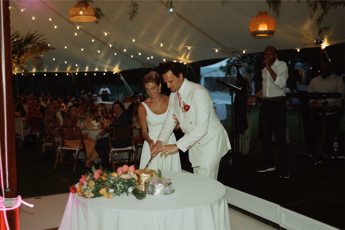 Couple cutting their cake inside the tented reception strung with fairy lights