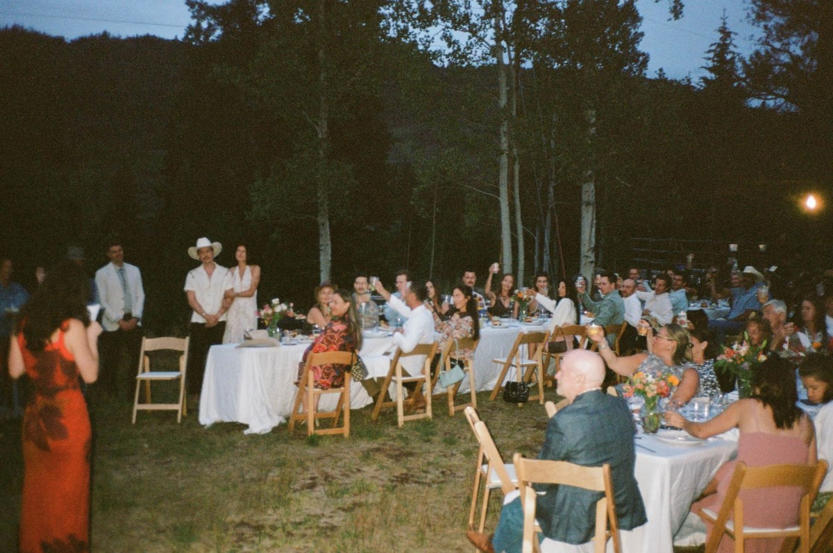 Guests toast at the long tables as dusk falls, shot on film at a mountain ranch among the aspens