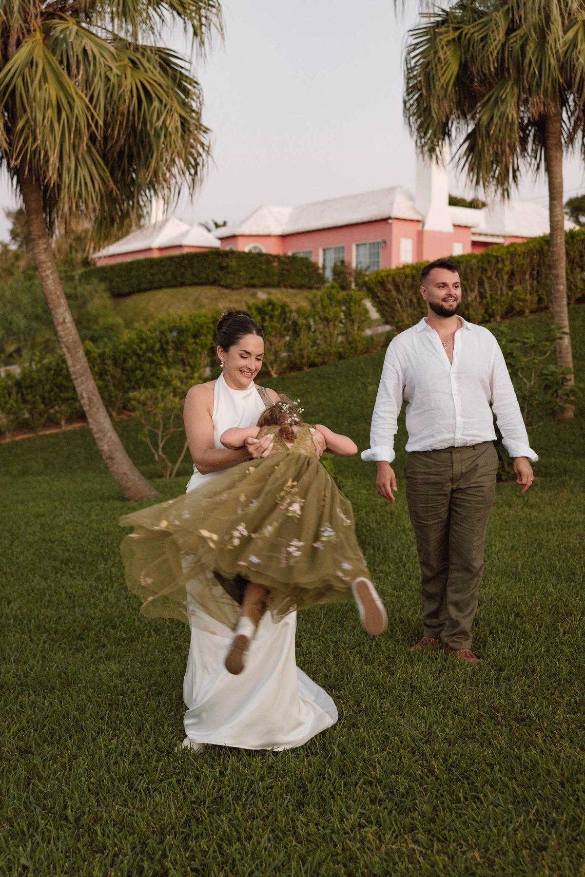 Bride and groom swinging the flower girl between them on the lawn