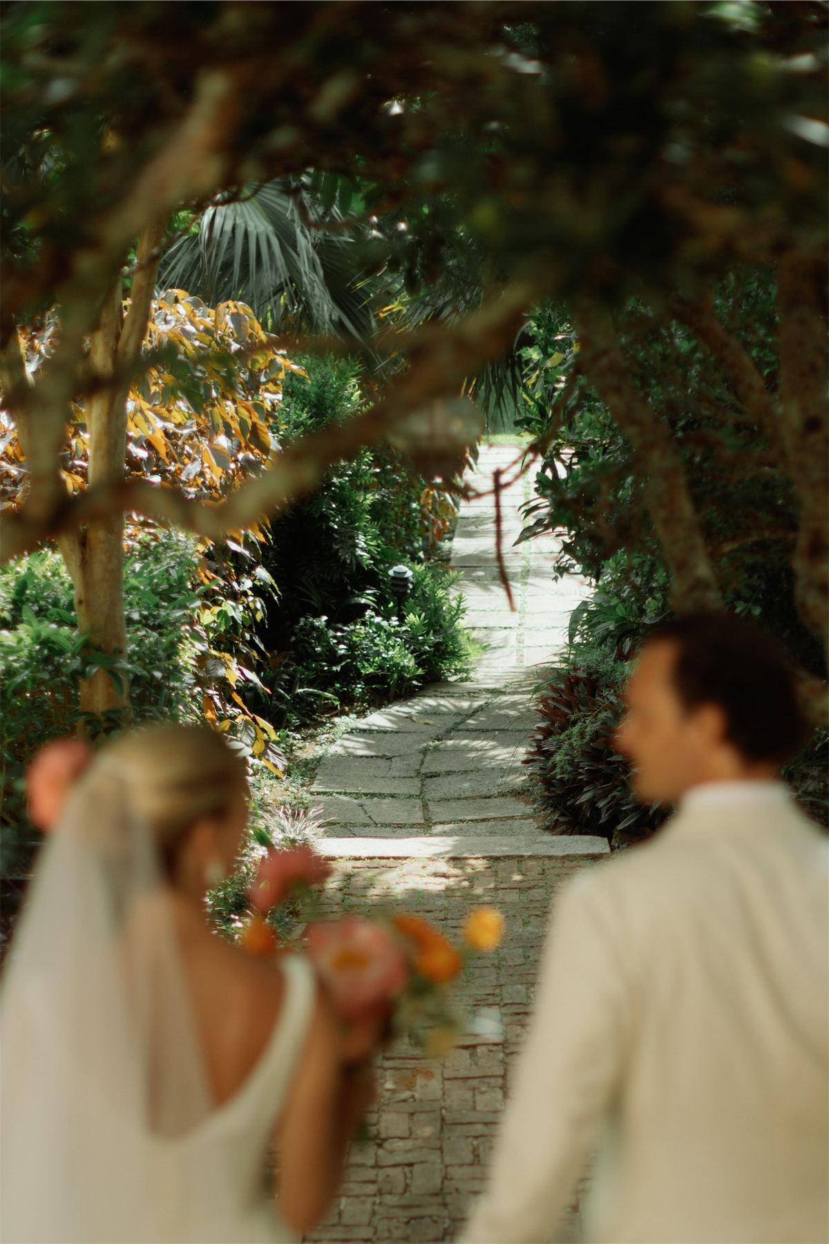 Bride and groom walking a shaded garden path lined with tropical planting