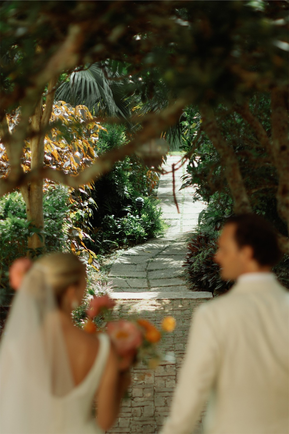 Bride and groom walking a shaded garden path lined with tropical planting