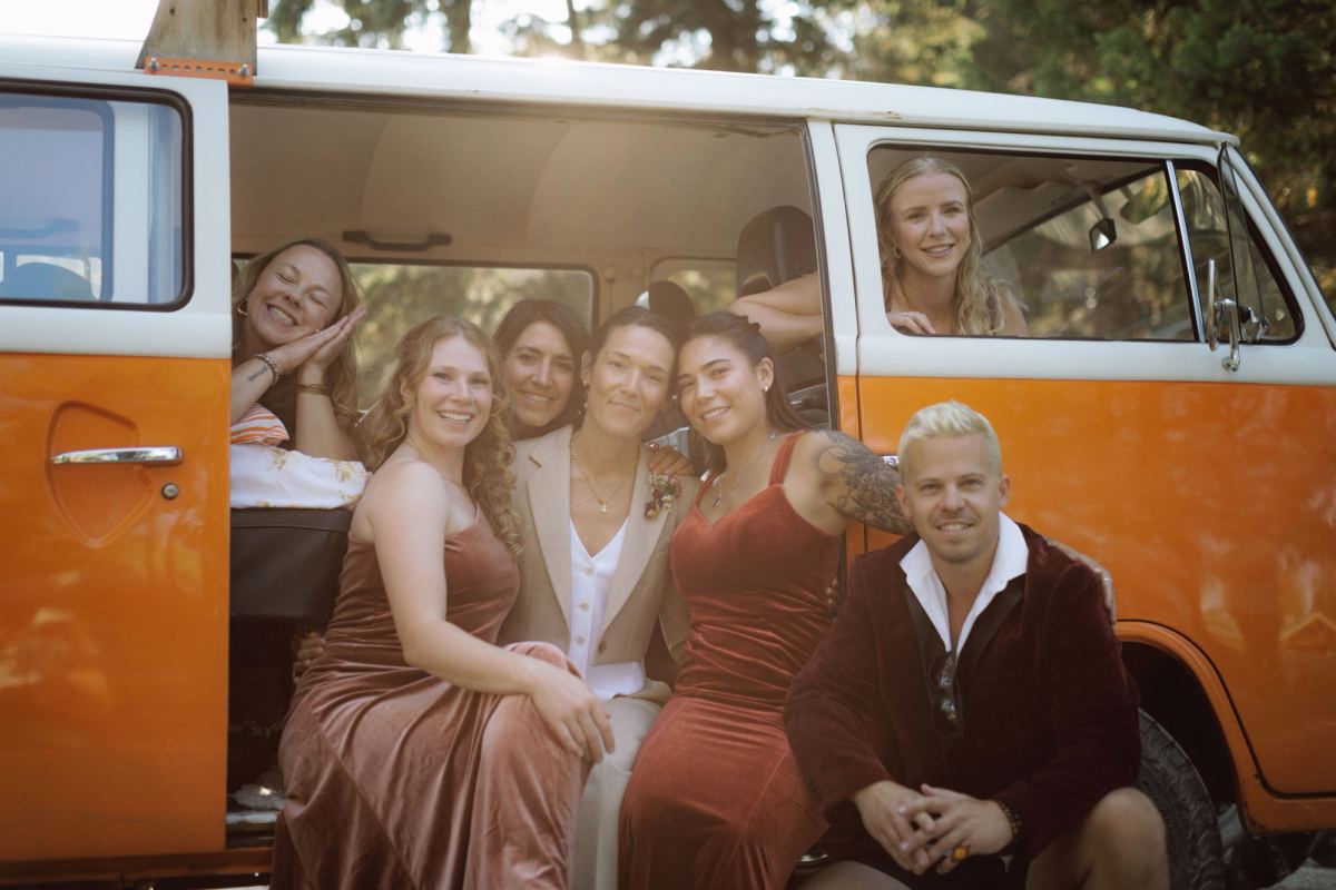 Bridal party in rust dresses piled into an orange VW camper van