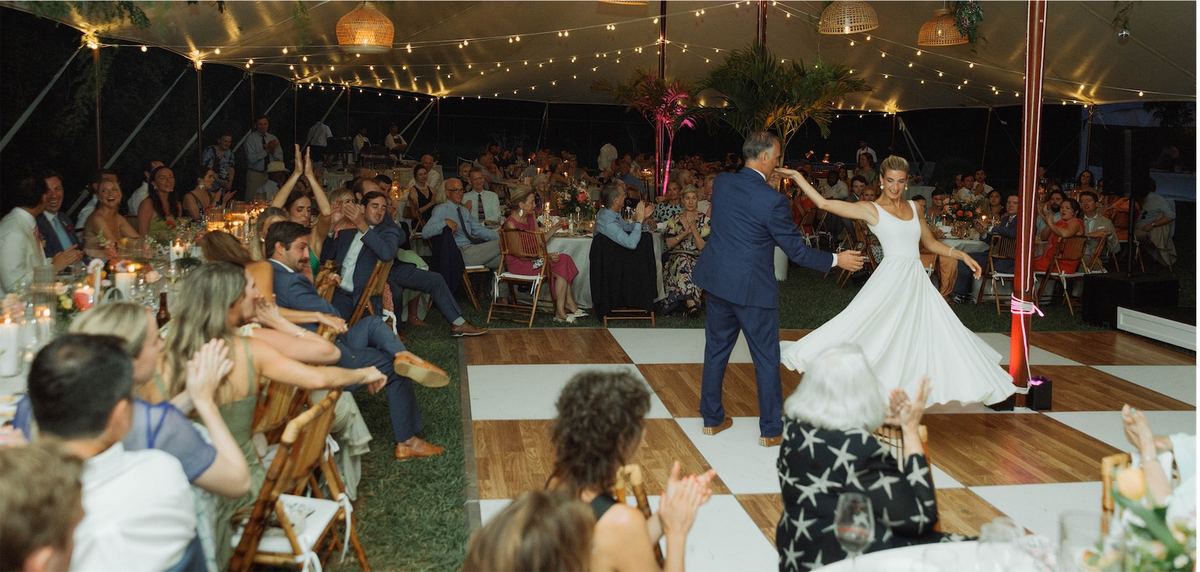 Bride dancing with her father on the checkerboard dance floor as guests cheer