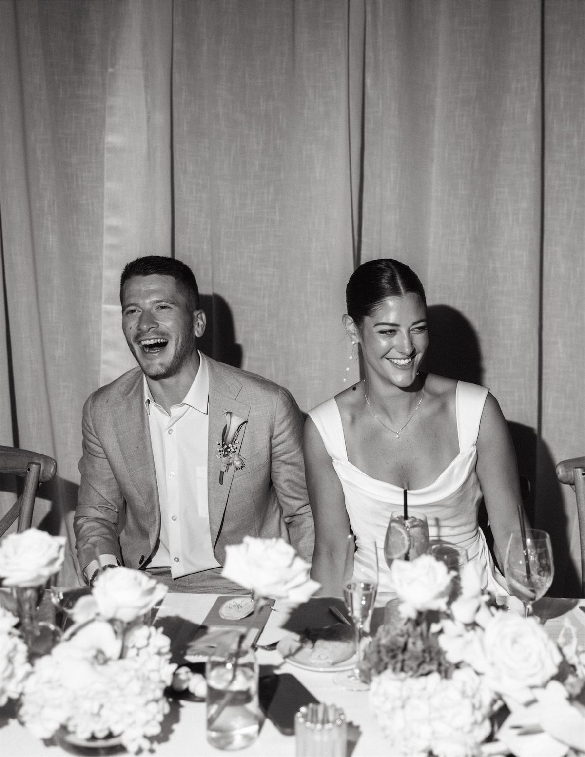 Black and white of the bride and groom laughing at the head table during speeches