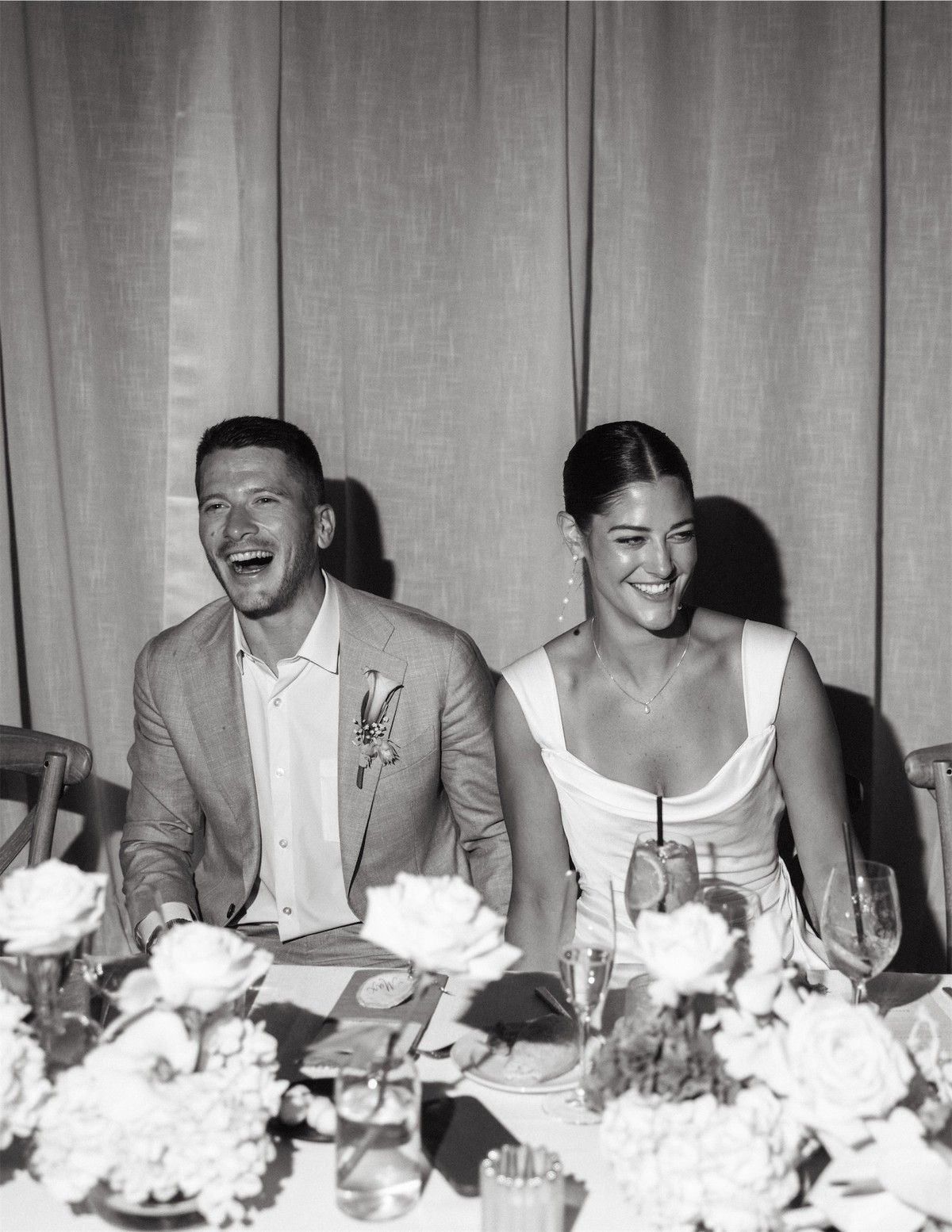 Black and white of the bride and groom laughing at the head table during speeches