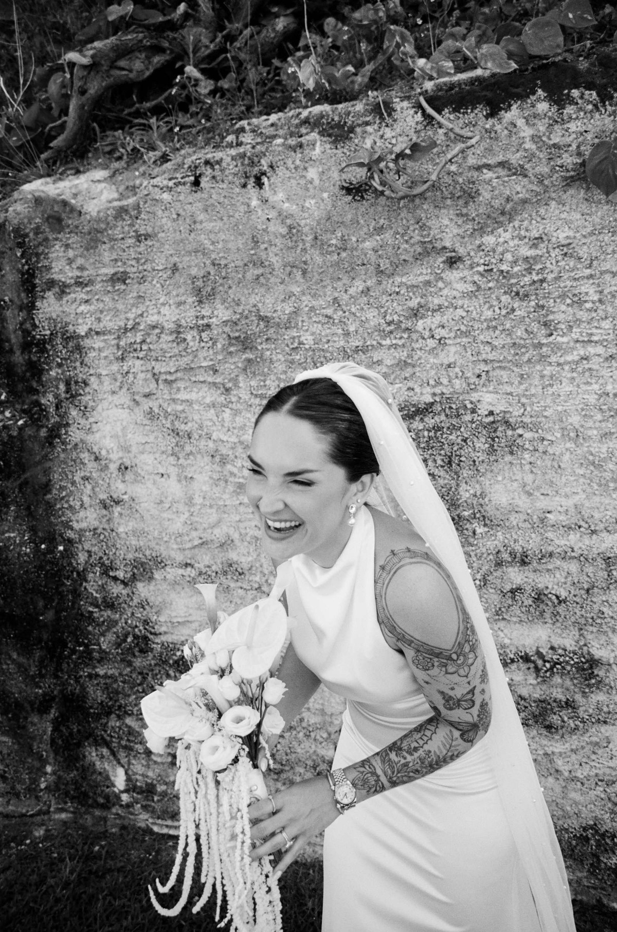 Black and white photograph of the bride laughing against a weathered Bermuda wall
