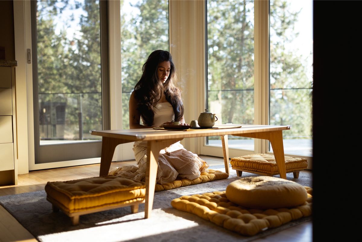 Woman seated on floor cushions at a low table in a sunlit lounge