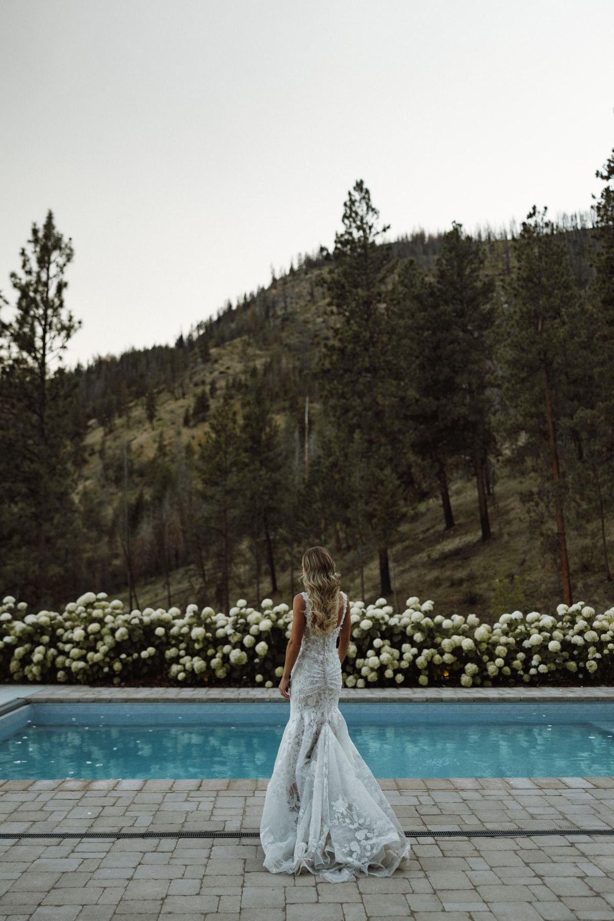 Bride walking beside the pool in her gown with the hills behind her