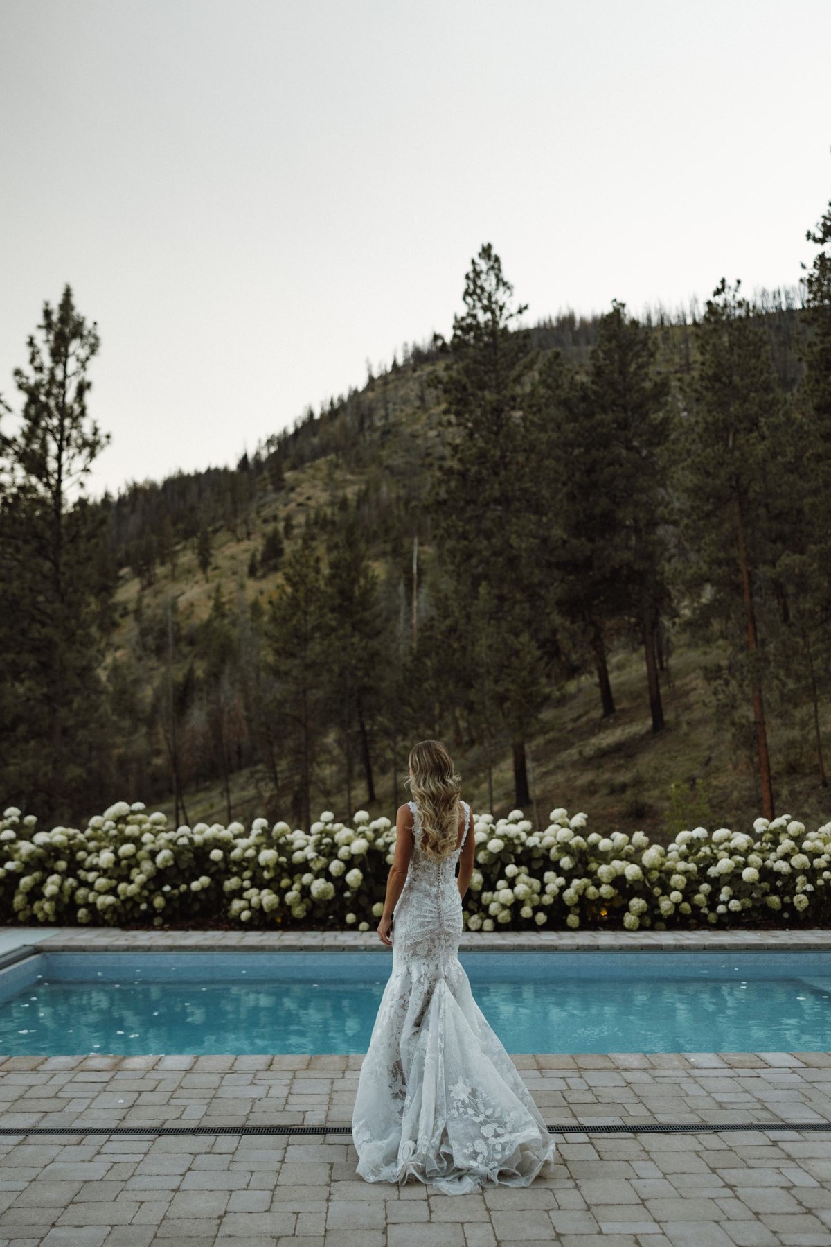 Bride walking beside the pool in her gown with the hills behind her