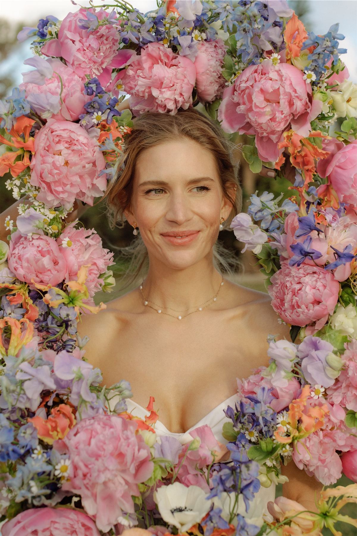 Bride smiling from inside a lush arch of pink peonies and sweet peas