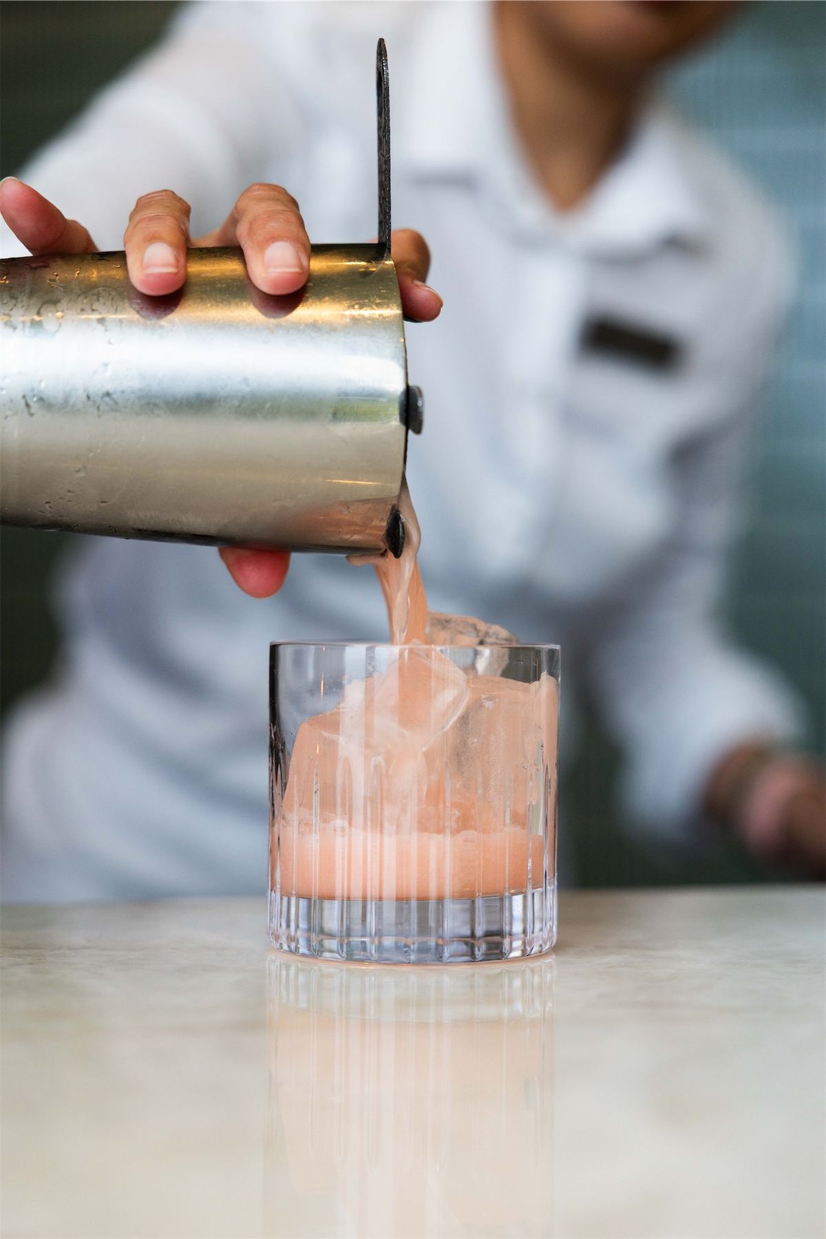 Bartender straining a pink cocktail into a rocks glass behind the bar
