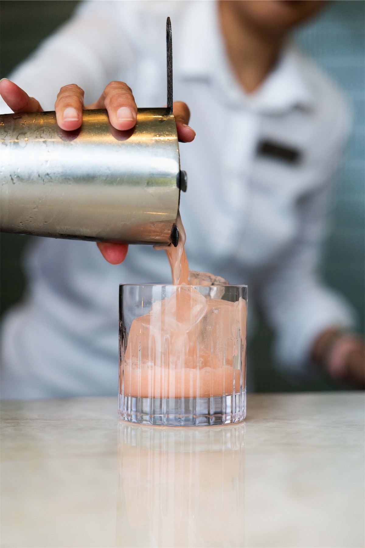 Bartender straining a pink cocktail into a rocks glass behind the bar