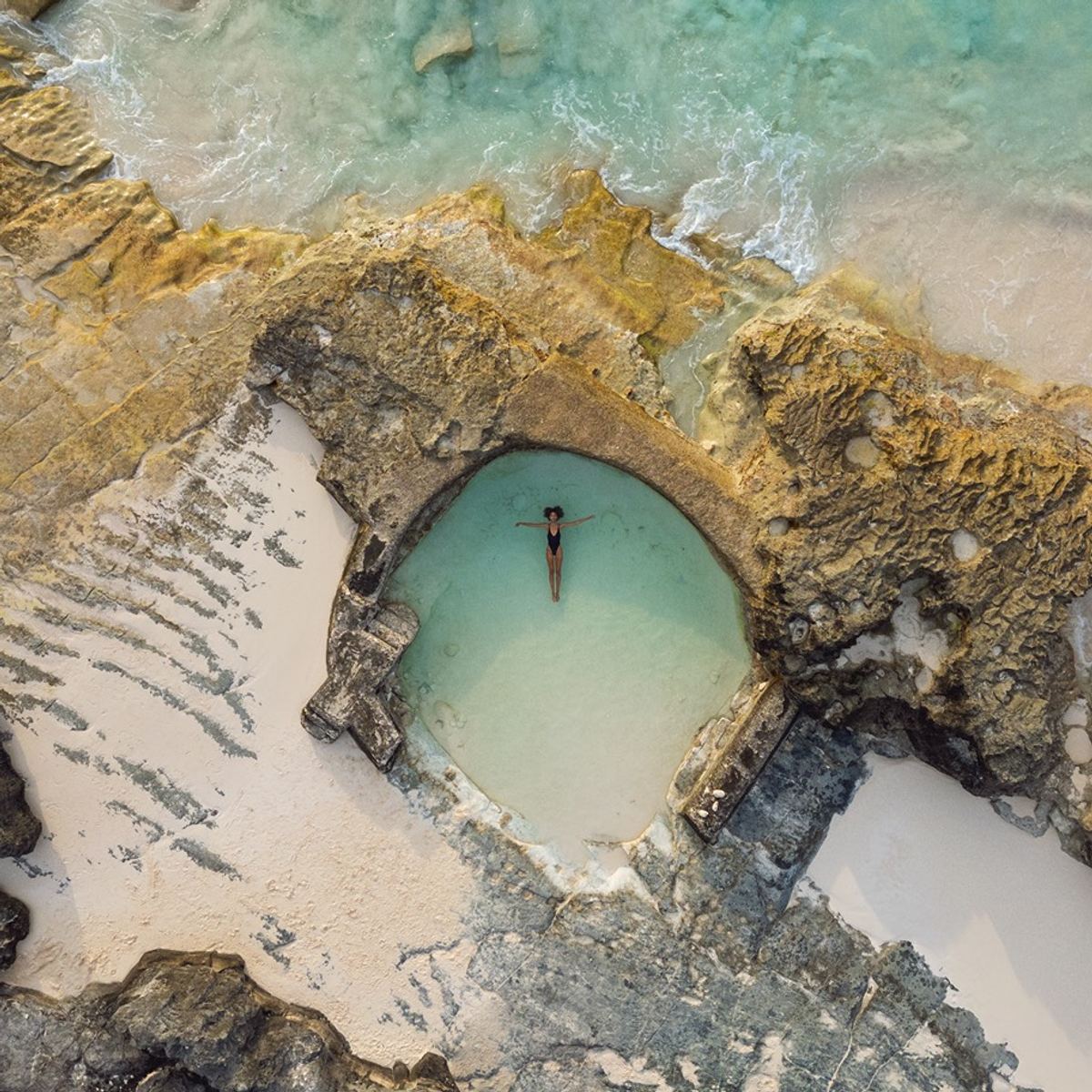 Aerial view of a swimmer floating alone in a turquoise natural rock pool