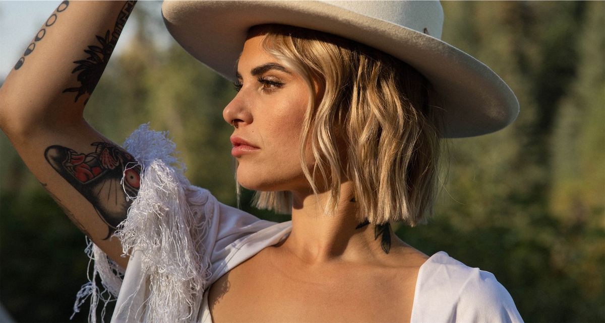 Bride in a wide-brimmed hat and fringed jacket looking out toward the trees