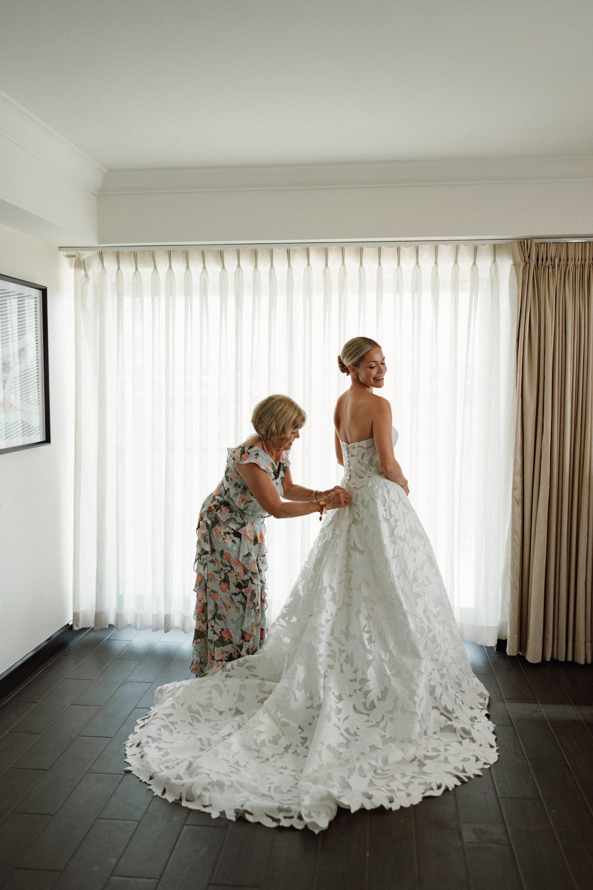 Bride being helped into her gown by her mother in soft window light