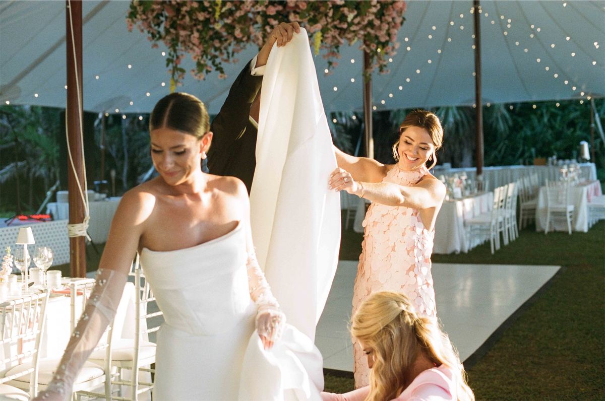 Attendants smoothing the bride's train under a flower-hung reception tent