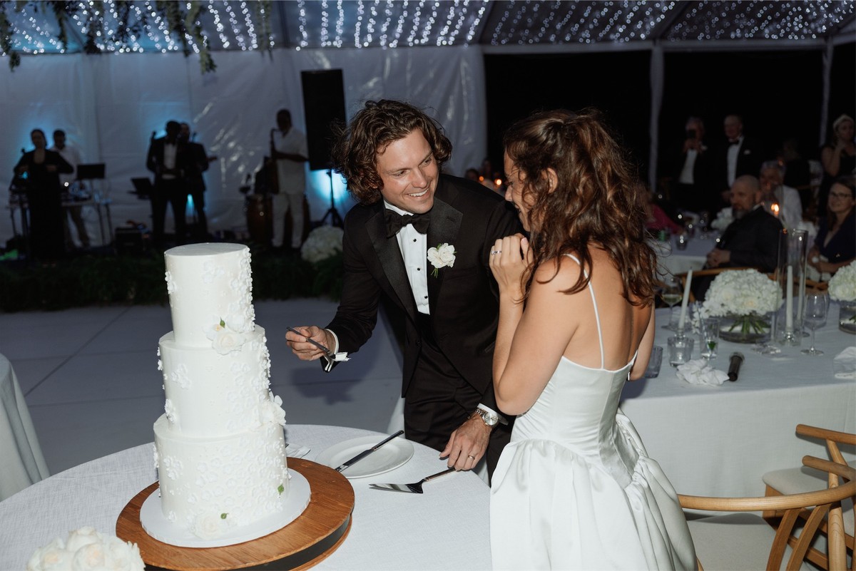 Bride and groom cutting a tiered white wedding cake inside the tented reception