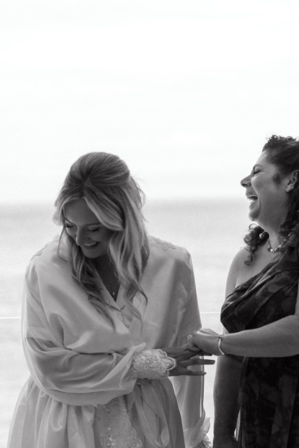 Black and white candid of bride and friend laughing during preparation