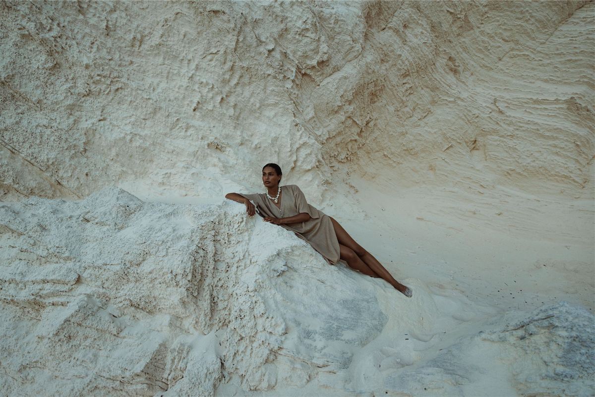 Model reclining across a white limestone outcrop in a matching linen set