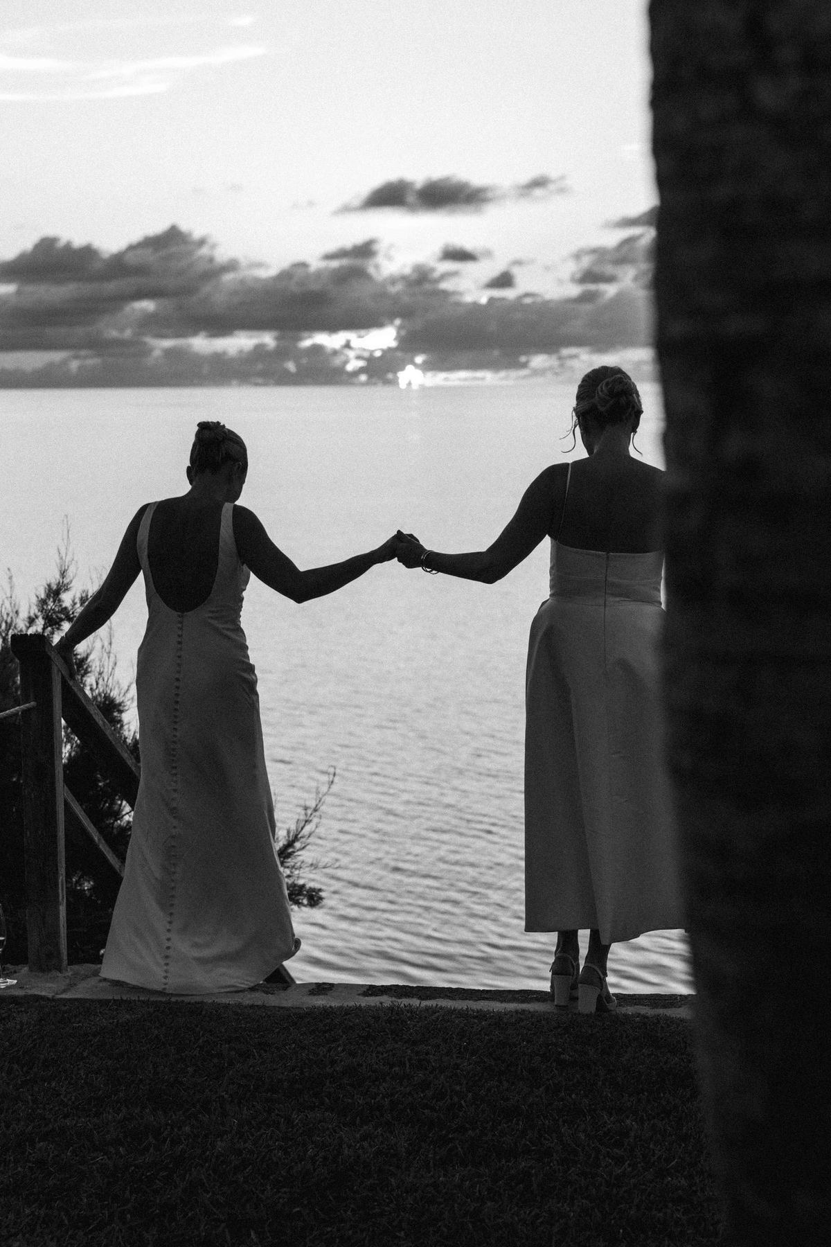 Black and white silhouette of two brides holding hands at dusk by the Bermuda water
