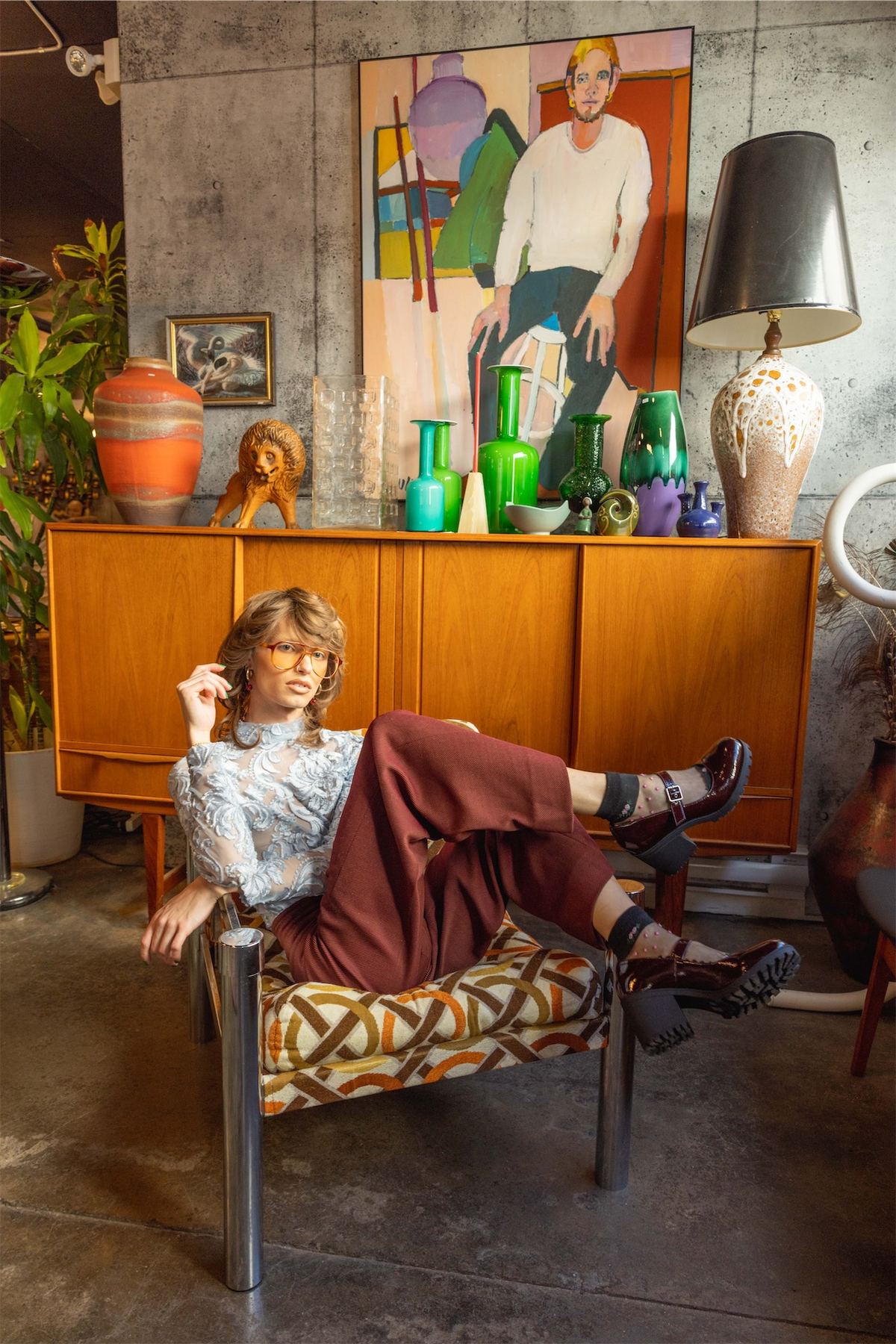 Model reclining in a vintage interior beside a teak sideboard and coloured glassware