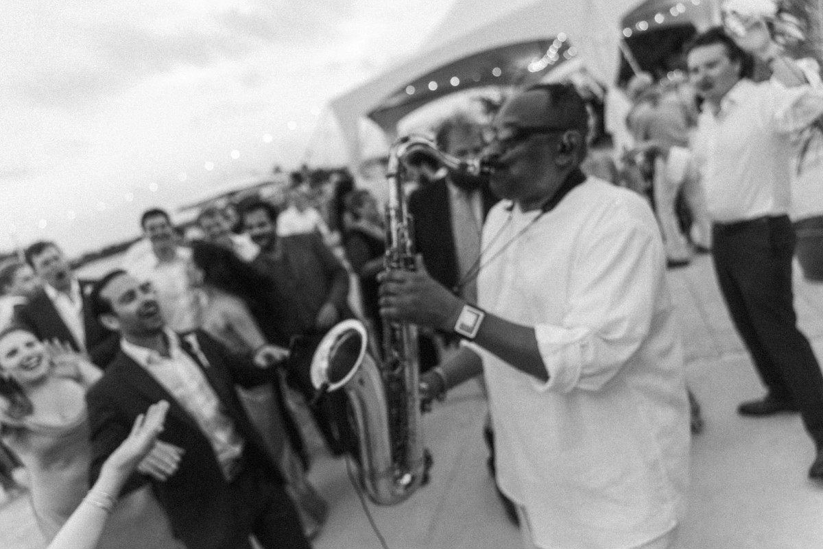 A saxophonist plays in the middle of the dancing crowd on Hawkins Island, Bermuda, black and white