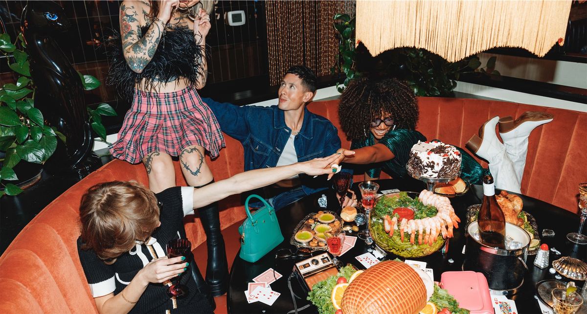Group of models lounging in a red diner booth surrounded by a spread of food