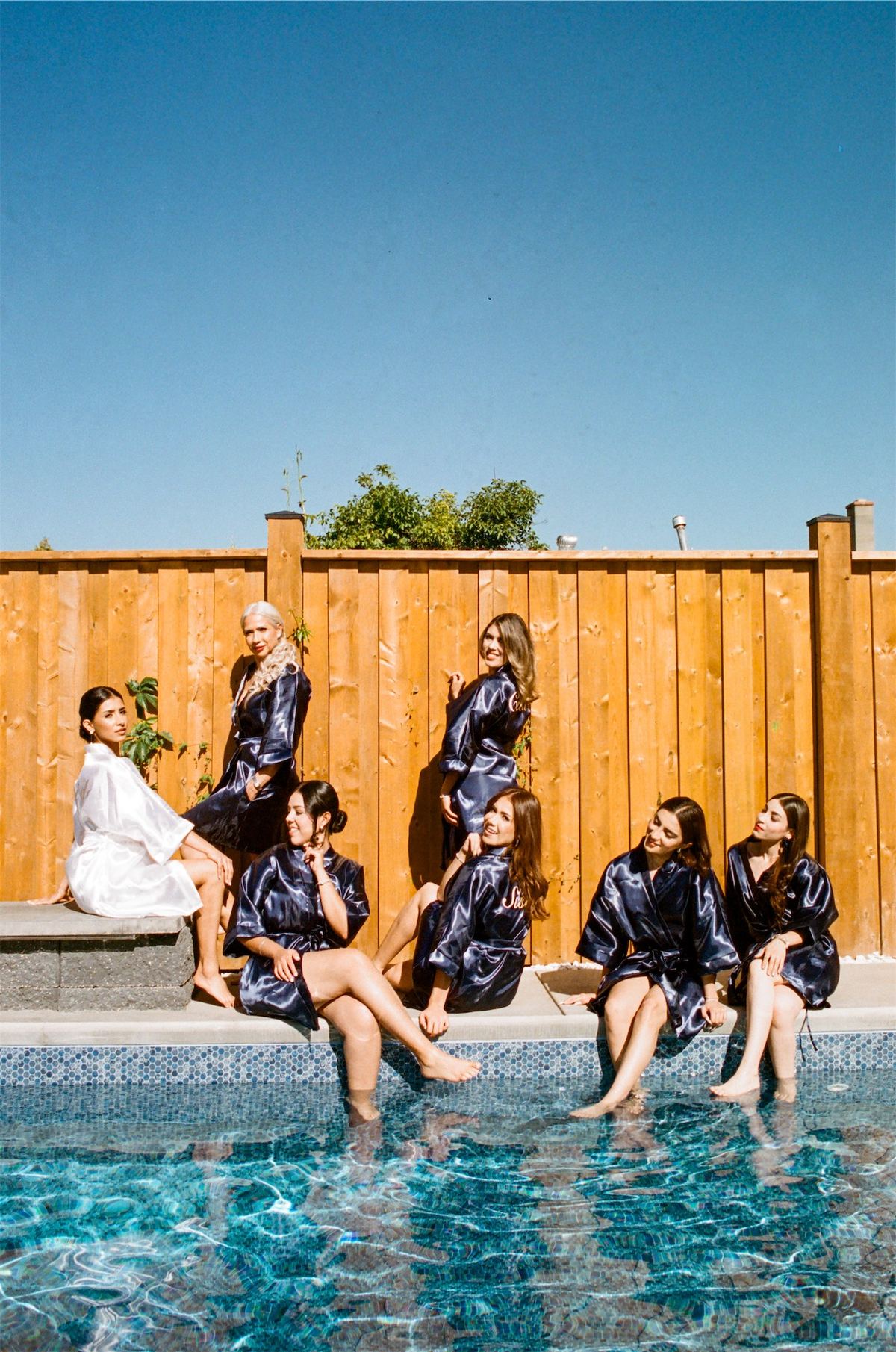 Bridesmaids in patterned robes sitting poolside with their feet in the water