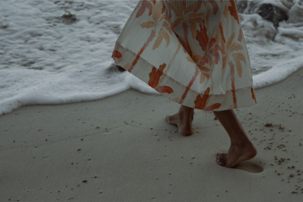 Cropped frame of a printed skirt and bare feet as a wave washes over the sand