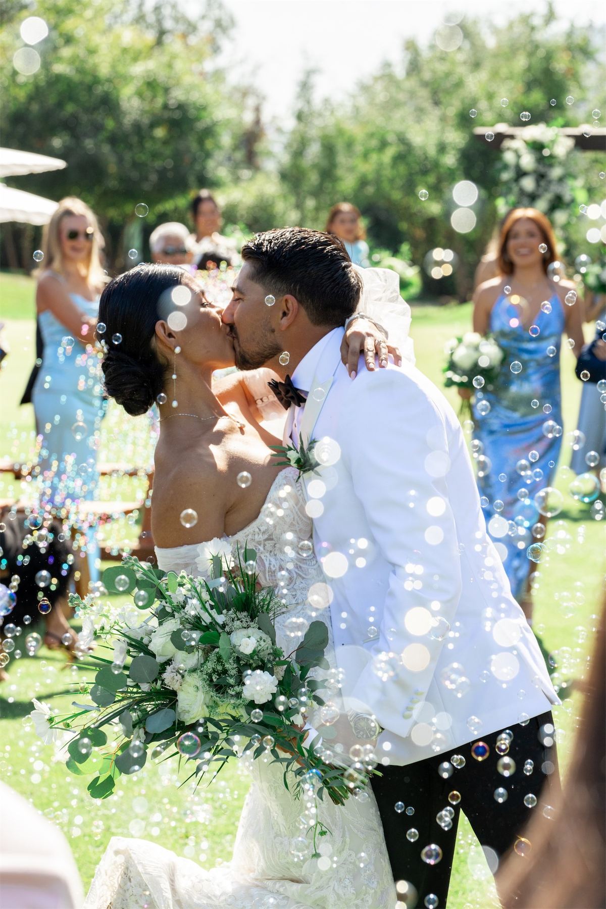 Couple kissing in a cloud of bubbles blown by guests on the lawn