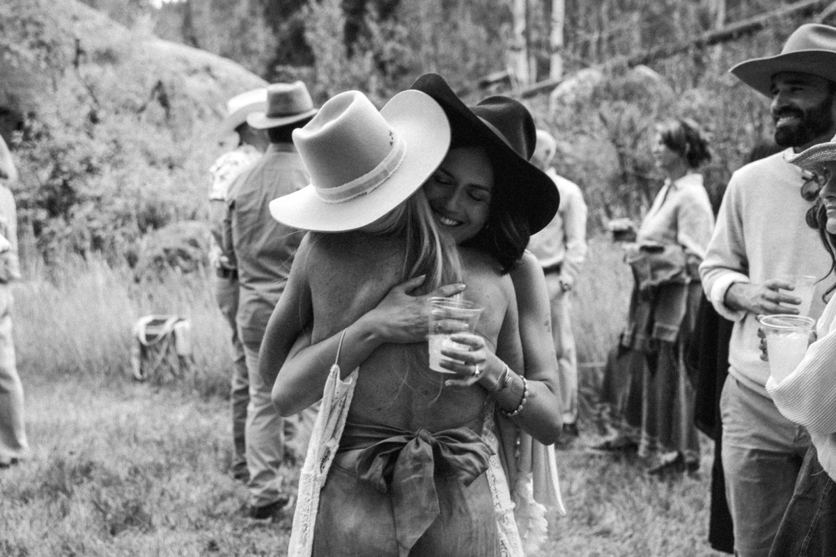 Devin hugs a friend in a cowboy hat at the welcome party at a mountain ranch among the aspens, black and white