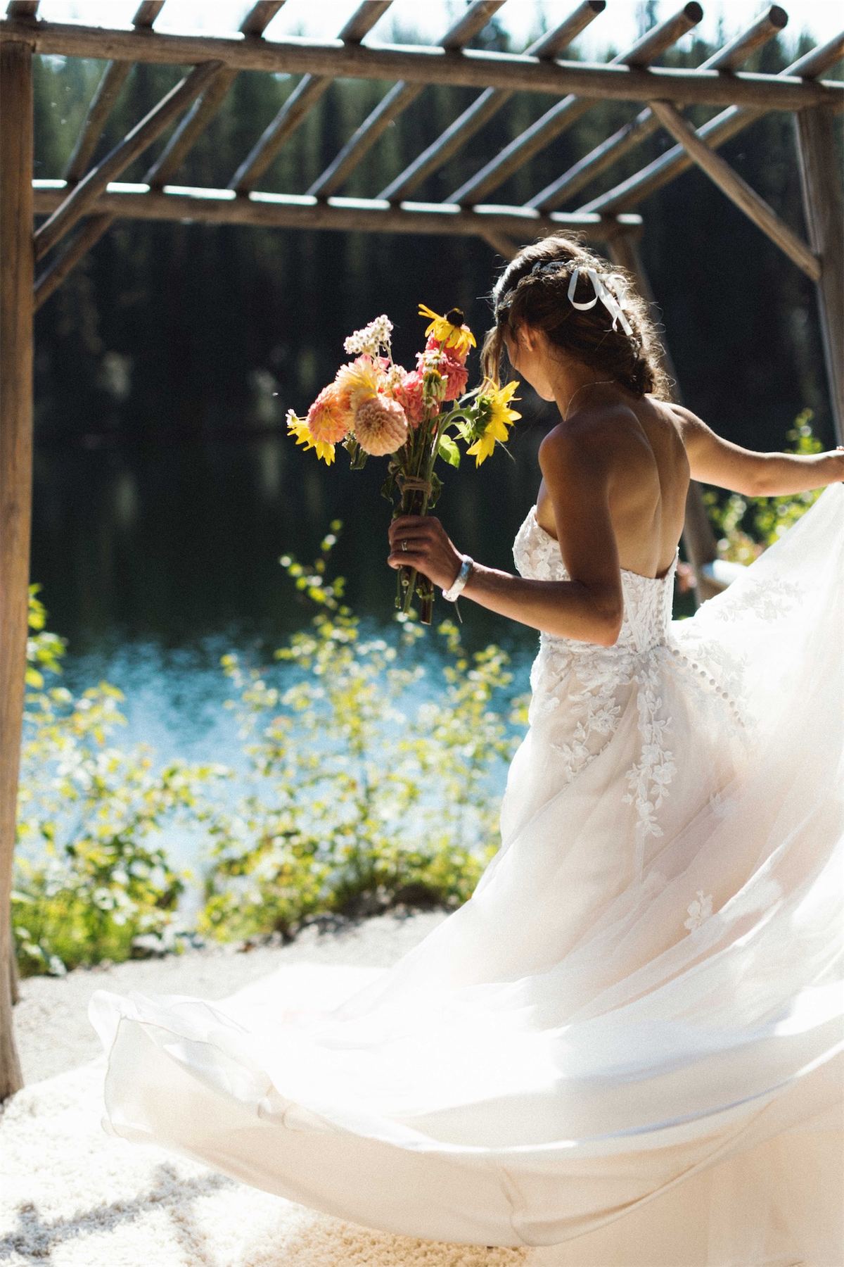 Bride by the lake with her gown fanned out, holding a dahlia bouquet