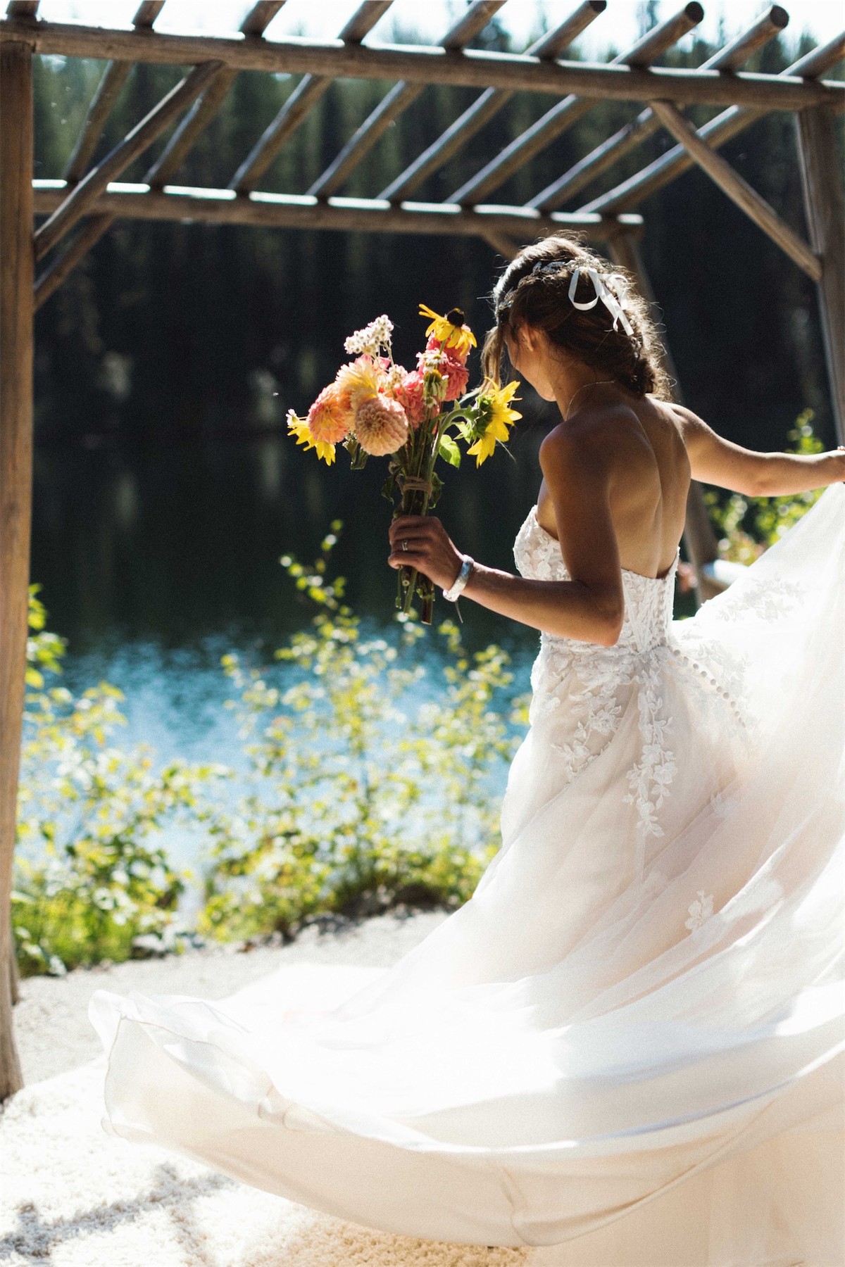 Bride by the lake with her gown fanned out, holding a dahlia bouquet