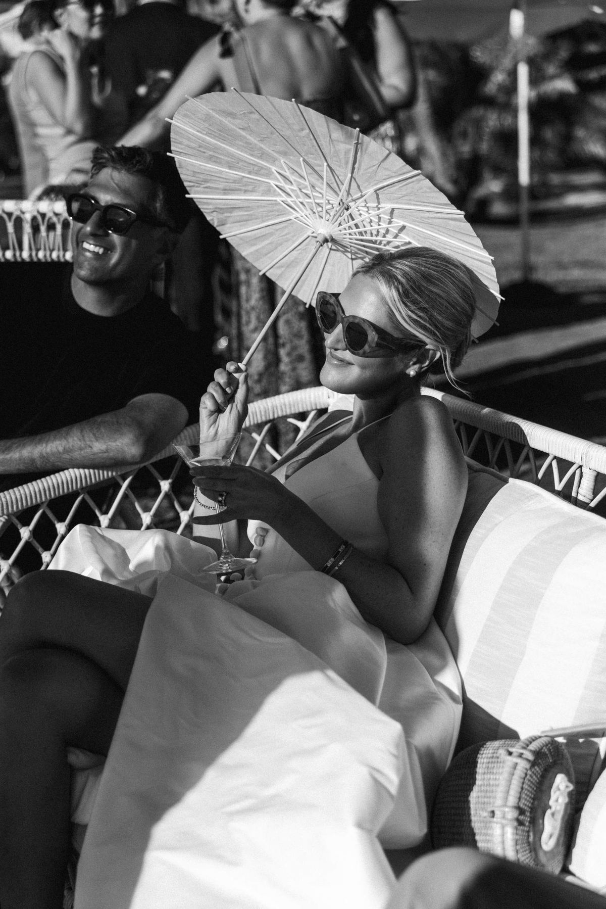 Black and white candid of guests laughing under a paper parasol