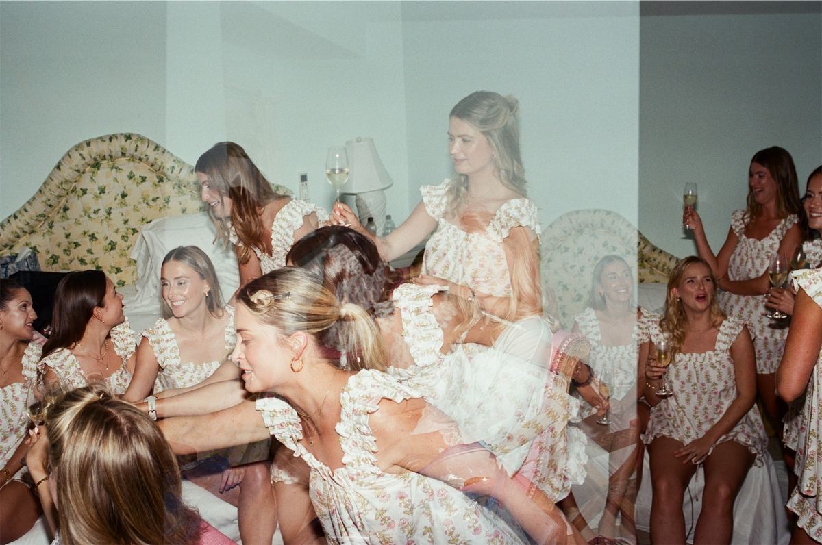 Bridesmaids in floral dresses piled together laughing while getting ready