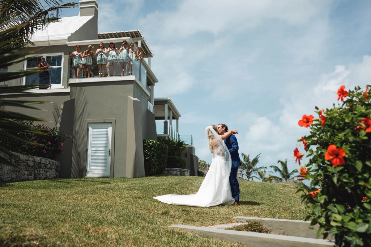 Paige and Cam embrace on the lawn after the first look as the bridesmaids look on on Hawkins Island, Bermuda