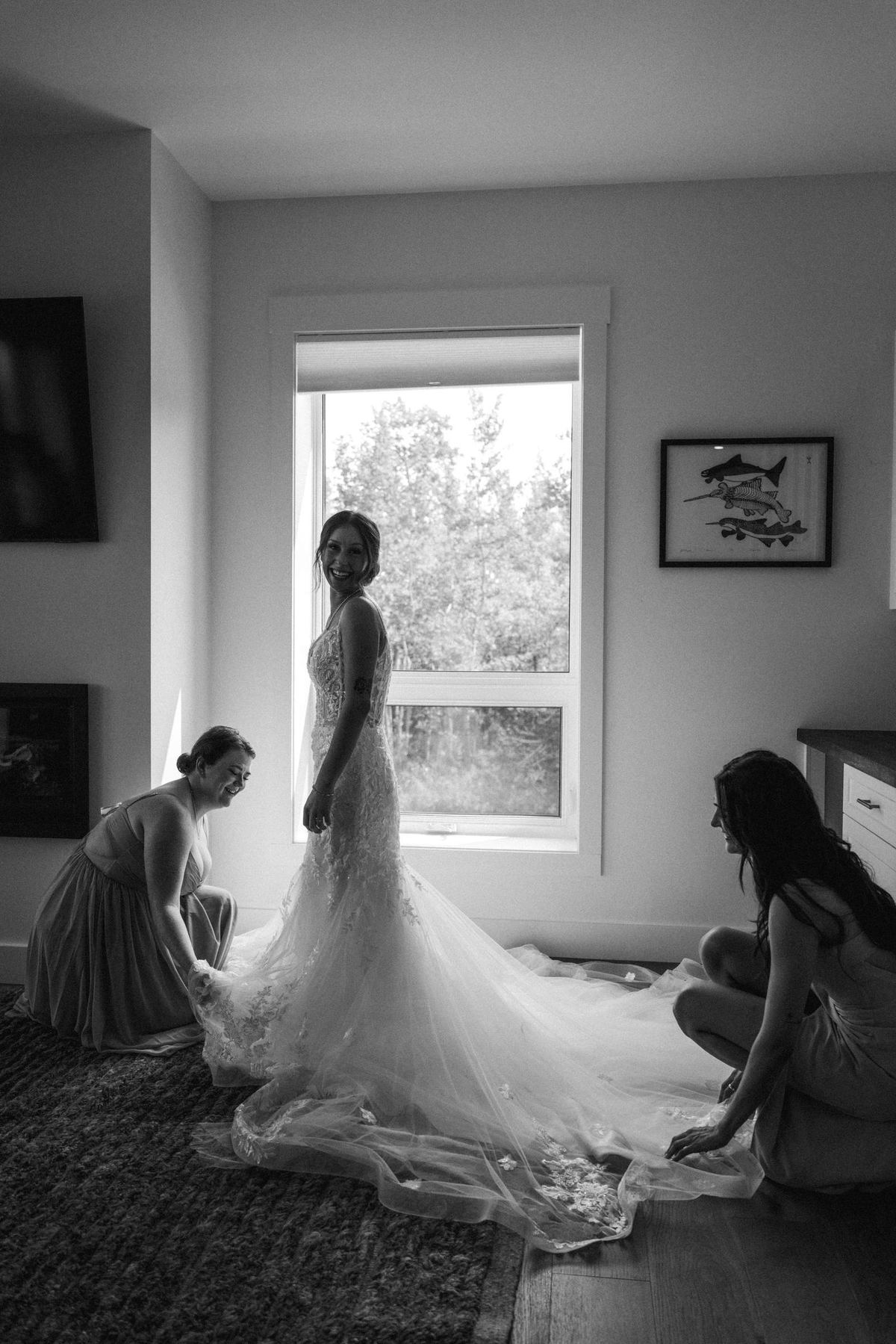 Black and white photograph of the bride being dressed with her train spread across the floor