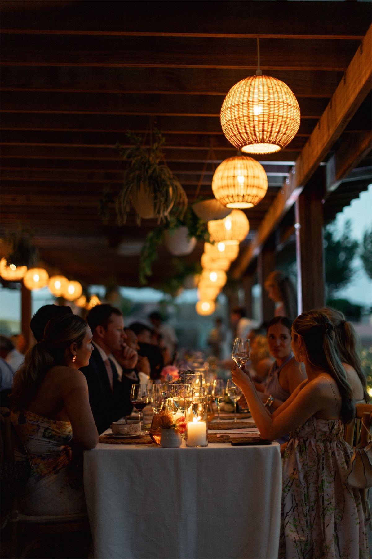 Candlelit reception dinner under woven lanterns on a covered seaside terrace