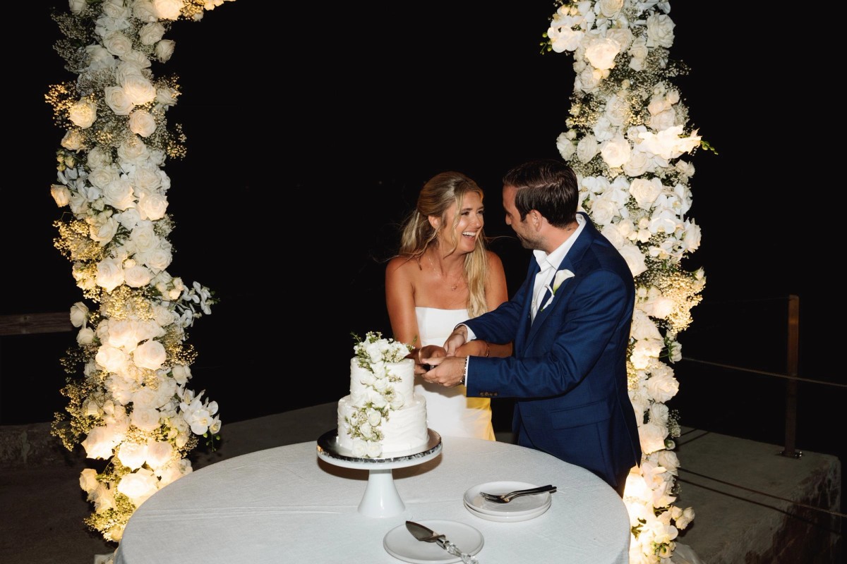 Paige and Cam cut the cake between the lit floral columns on Hawkins Island, Bermuda
