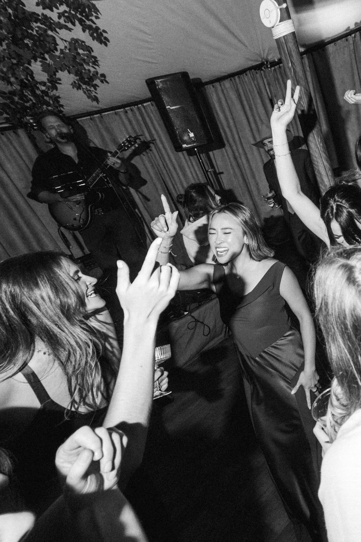Bridesmaids dance with arms raised under the tent at a mountain ranch among the aspens, black and white