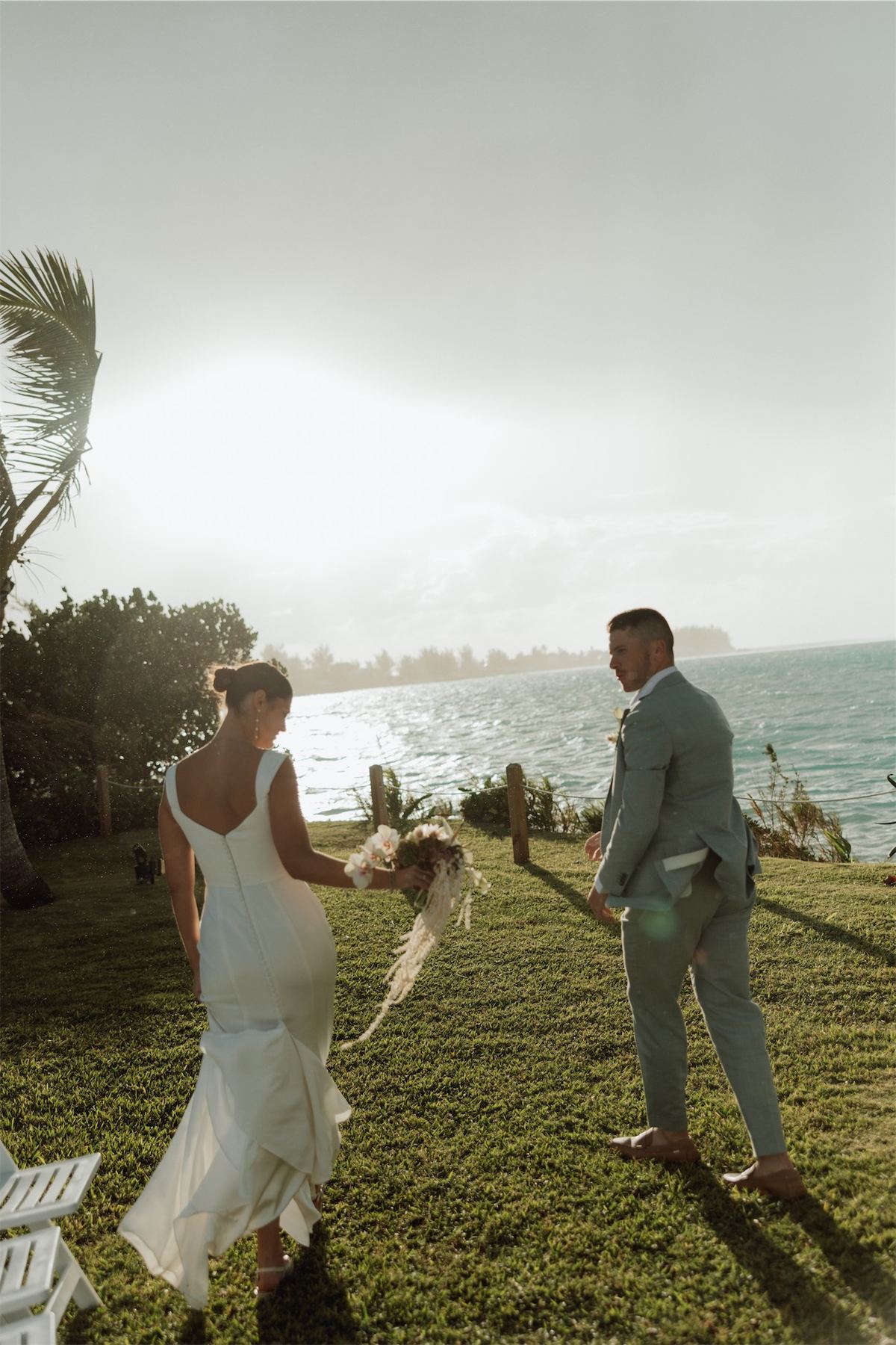 Bride and groom holding hands on a misty lawn above the sea