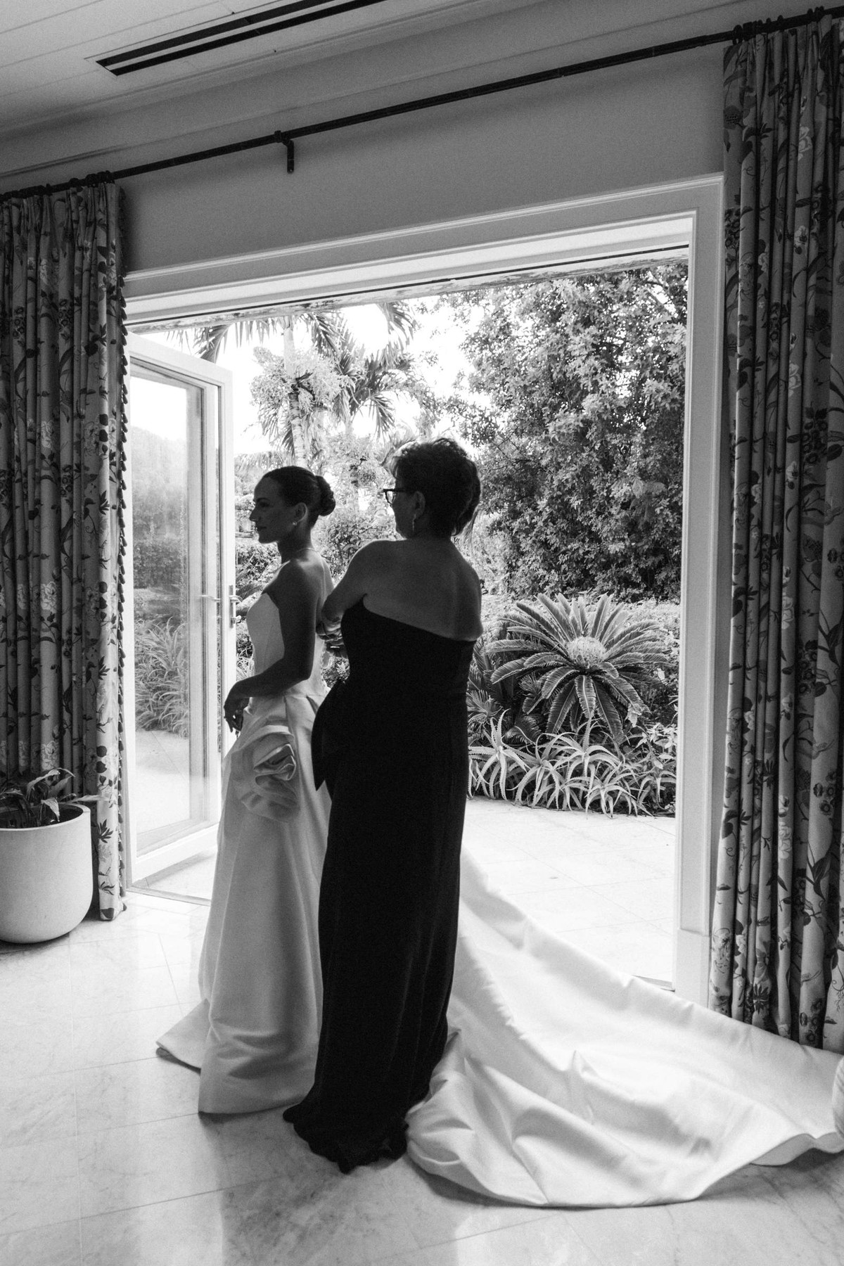 Mother buttoning the bride into her gown by open garden doors at Rosewood Bermuda, black and white