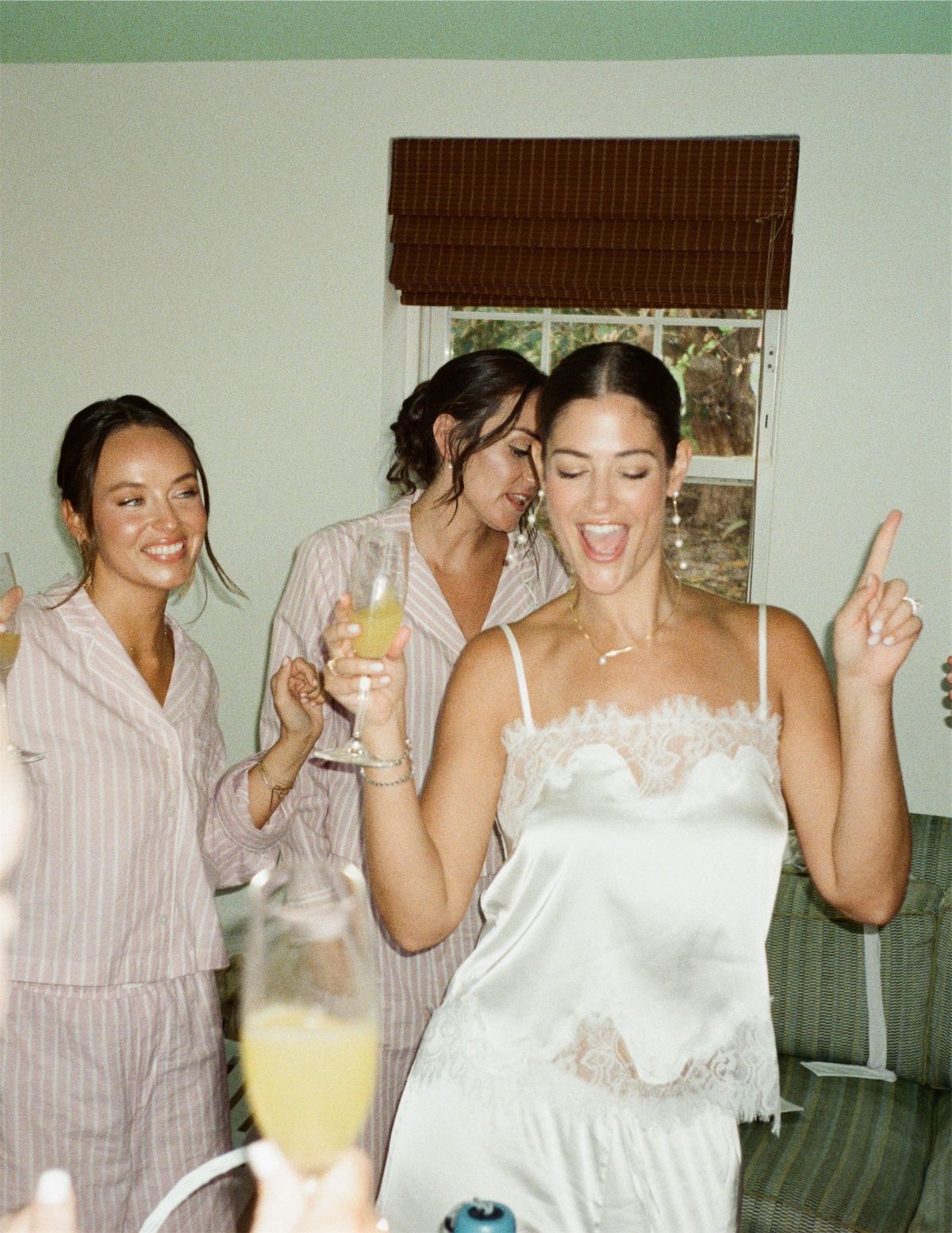 Bridesmaids in pyjamas laughing over mimosas the morning of the wedding