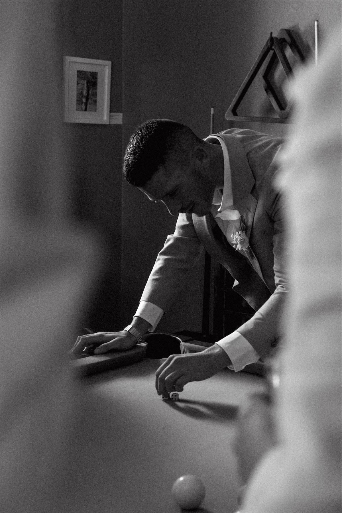 Black and white of the groom leaning across the pool table to line up a shot
