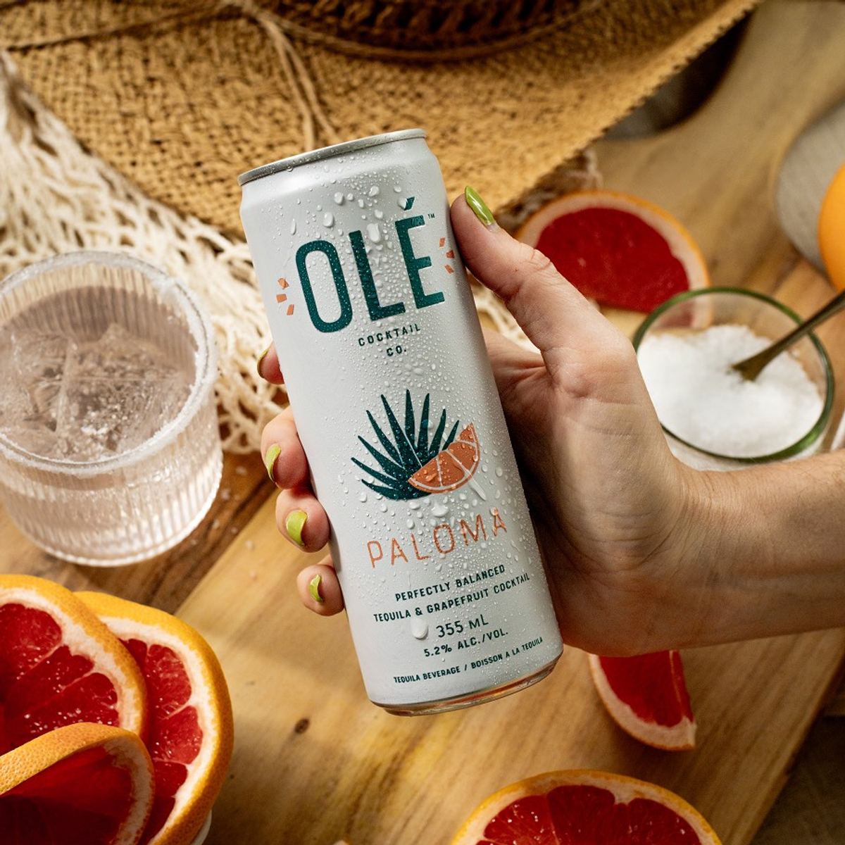 Model holding the paloma can above a table of sliced grapefruit, salt and ice